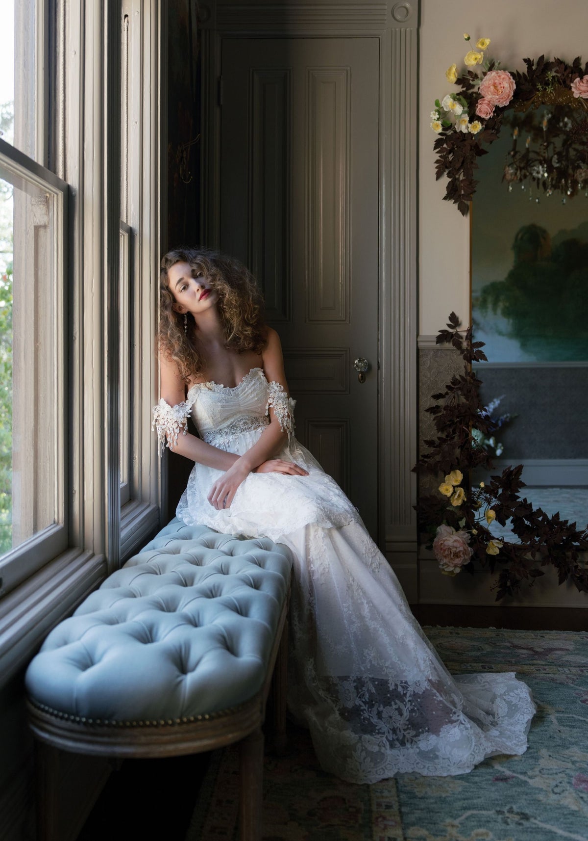 Bride seated by a window in the Amourette lace wedding dress with draped lace sleeves