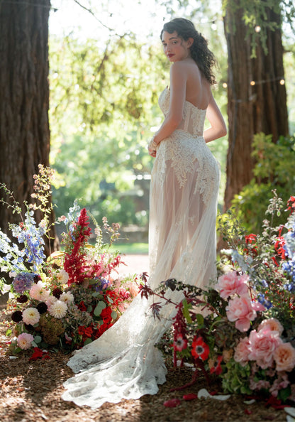 Back view of the Narcisse sheer chiffon wedding dress with floral embroidery among garden flowers