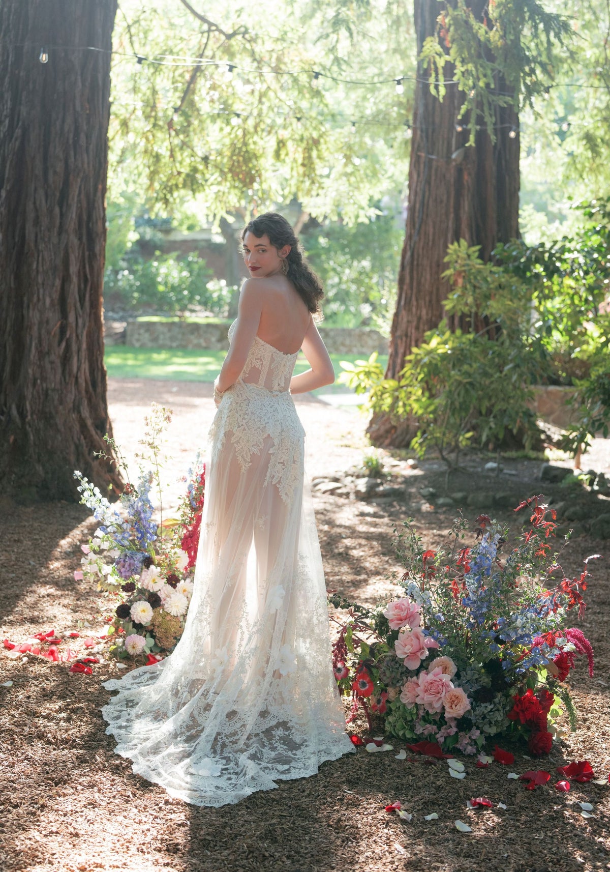 Narcisse sheer lace wedding dress with scalloped lace train spread among flowers