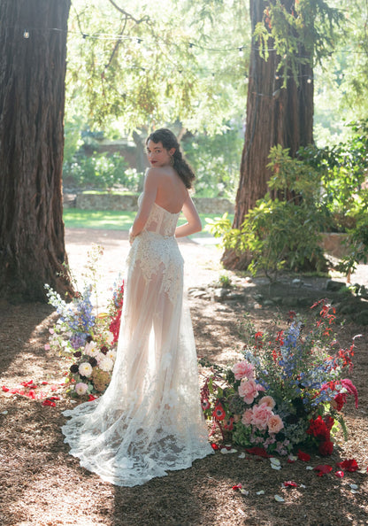 Narcisse sheer lace wedding dress with scalloped lace train spread among flowers