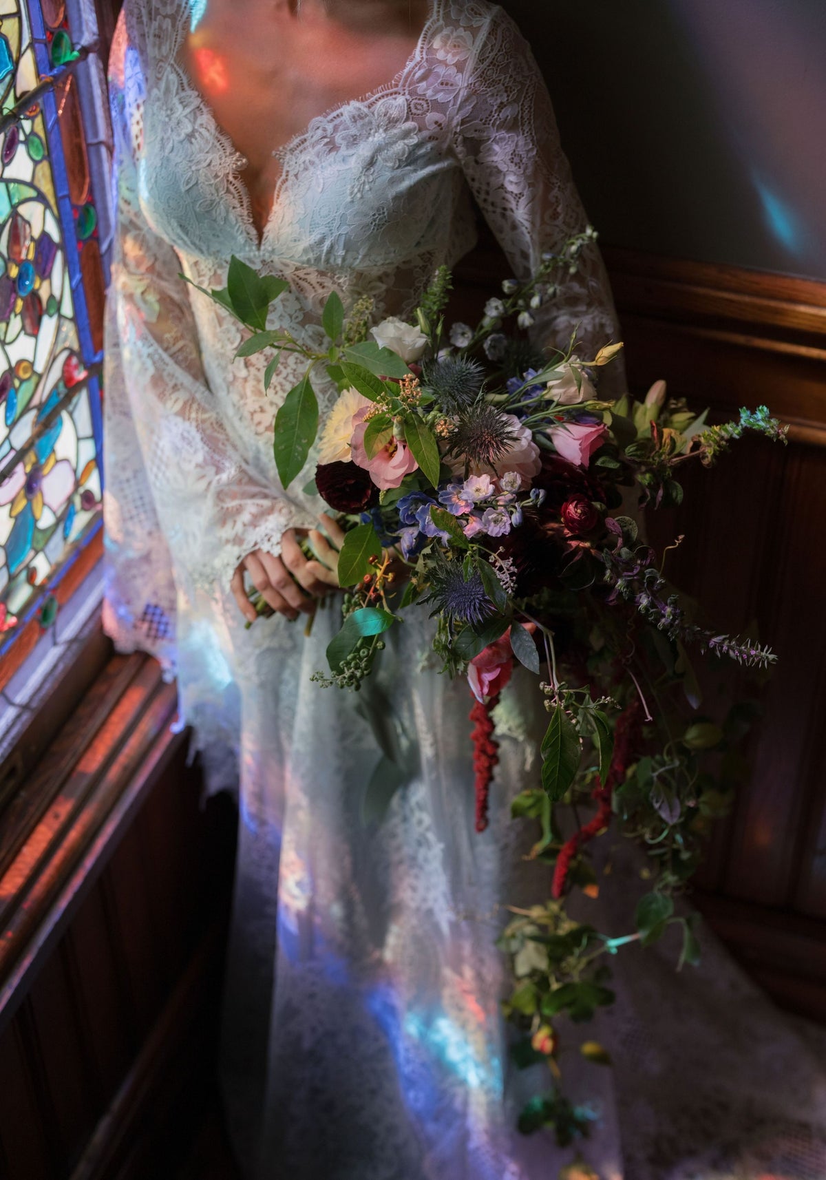 Bride holding a garden bouquet in the Serenade lace wedding dress beside a stained glass window