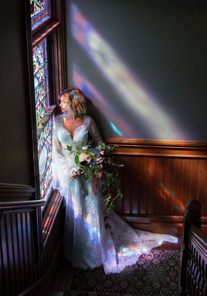 Bride in the Serenade bell sleeve lace wedding dress by a stained glass window at the Rhine House, Beringer Vineyards
