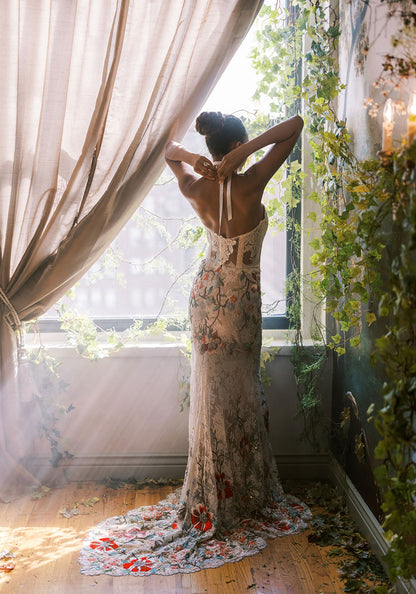 Bride in a colorful, embroidered gown tying her luxe halter straps, with rich floral detailing.