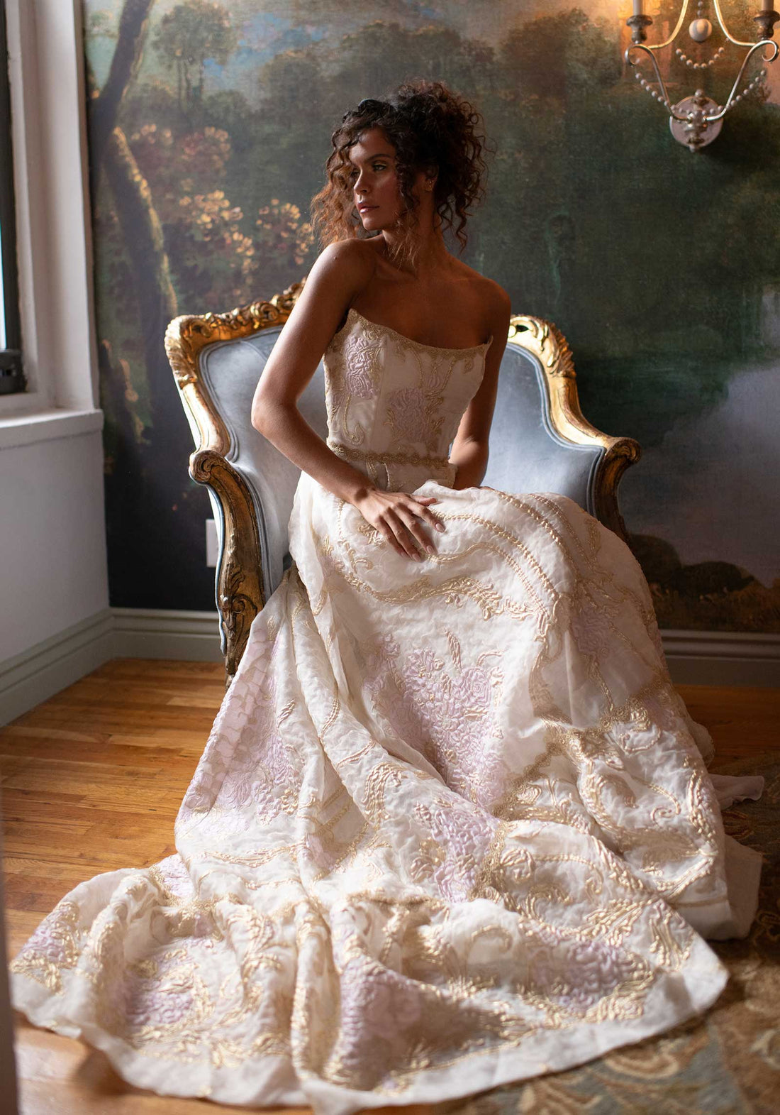Bride seated in romantic setting in Couture wedding dress with gold embellishments and lace trims