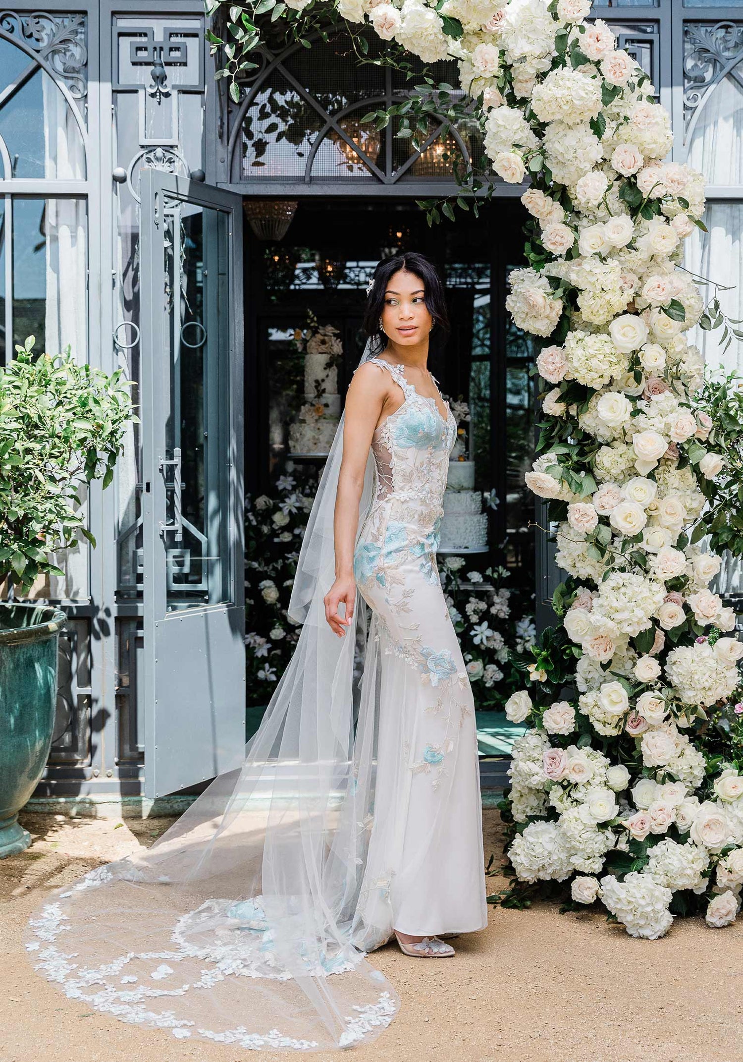 Model in Odessa Blue Wedding Dress in front of White Wedding Floral Arrangement